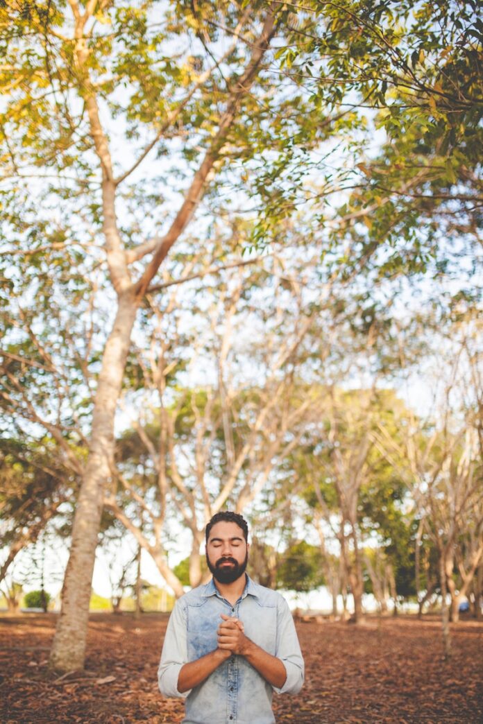 Photo by Naassom Azevedo man with eyes closed and clasped hands in front of chest under green tree