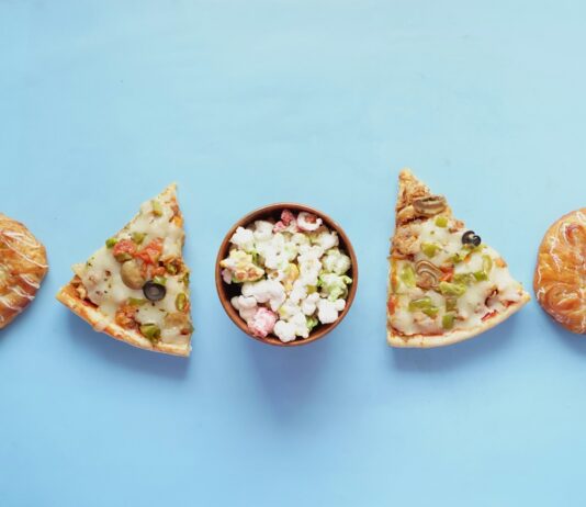 “아무거나 먹다간 큰일 납니다”…스트레스가 부르는 폭식, 식단으로 끊어내는 법 a bowl of popcorn and a slice of pizza on a blue background