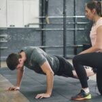 집에서도 쉽게 시작하는 근육 건강, 일상 속 탄탄한 습관이 열쇠 Man doing push-ups with a trainer spotting him.